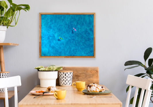 Modern dining nook with wooden table, plants, and framed aerial surf art on wall