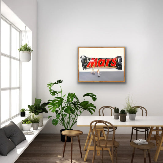 Framed pop art print of a large Mars bar with painter figure, displayed in a modern dining room.