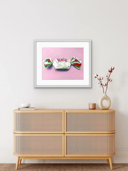 Framed pop art print of a Minties lolly on a pink background above a rattan cabinet