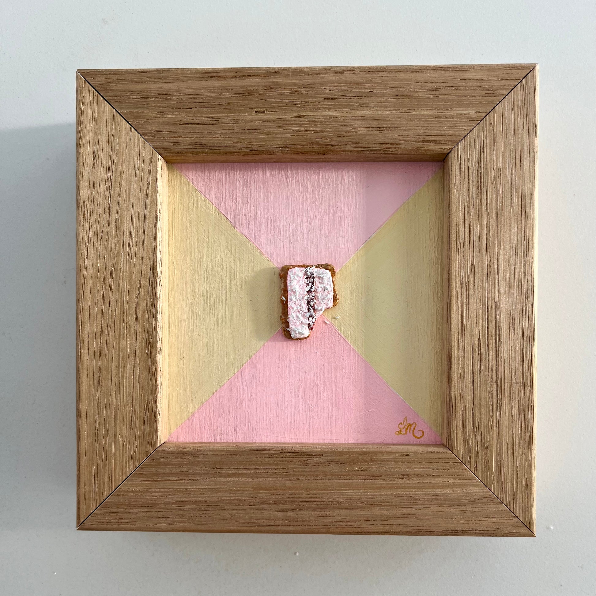 Wooden frame with geometric pink and gold interior on a light gray background with a iced vovo in 3D in the centre