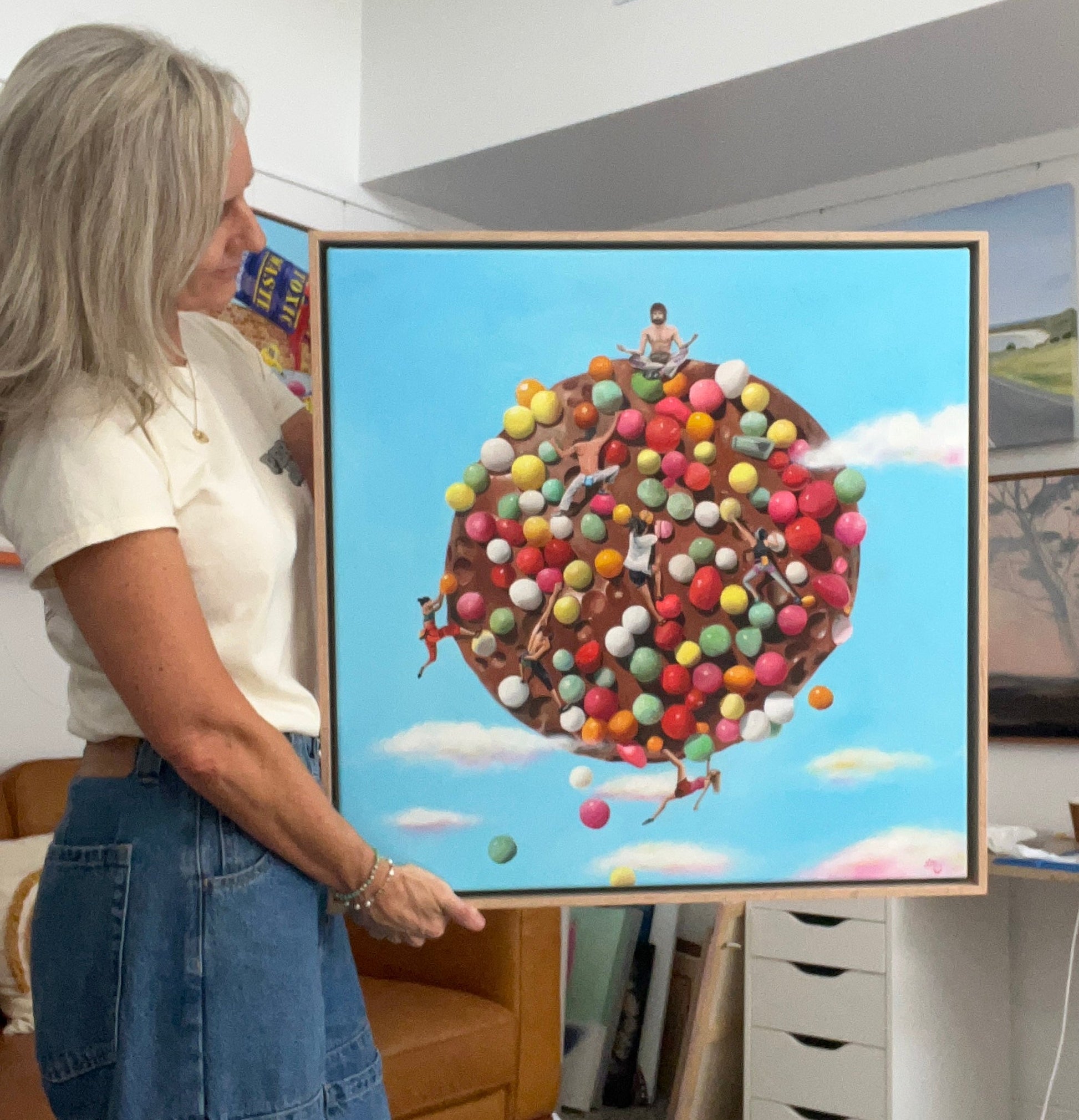 Leonie McIntosh holding a framed artwork of a freckle with hundreds and thousands and people on top.