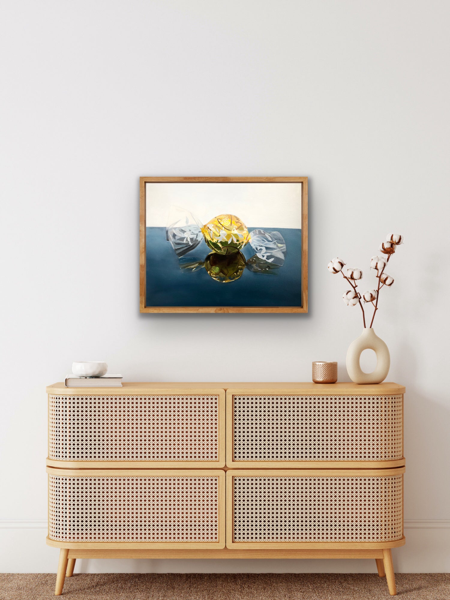 Framed pop art painting of a yellow wrapped candy displayed above a modern wooden sideboard.